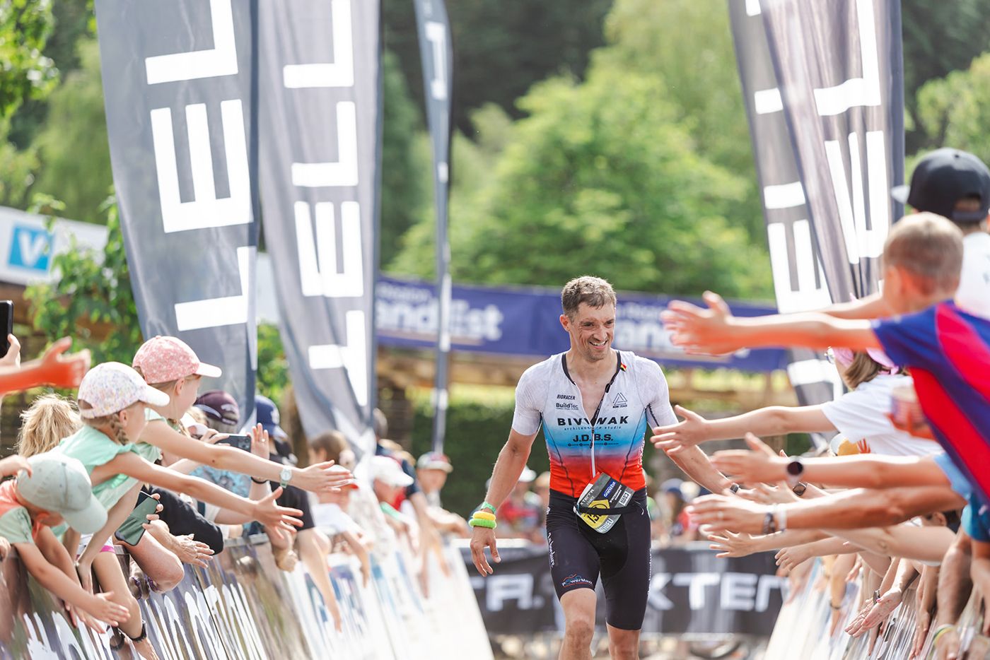 Mathis sous l’arche XTERRA, les spectateurs tendent les mains vers un finisher